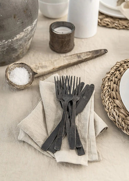 Table setting with black cutlery, candle, and ceramic bowl on a neutral background