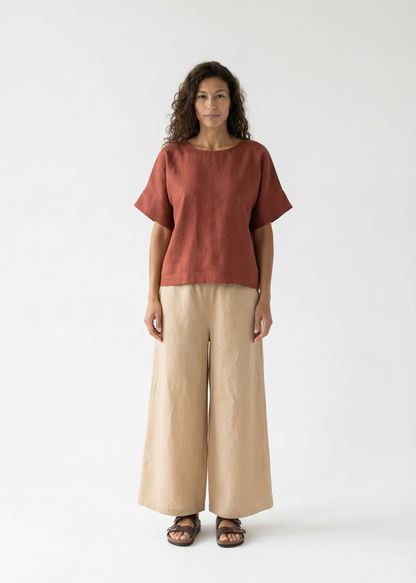 Woman wearing a rust-colored top and beige pants on a white background