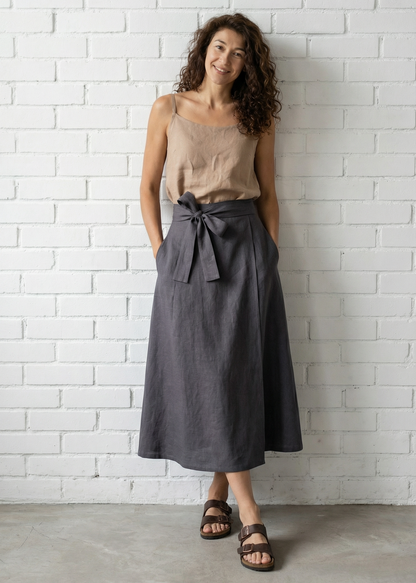 Woman wearing a beige top and gray skirt against a white brick wall.