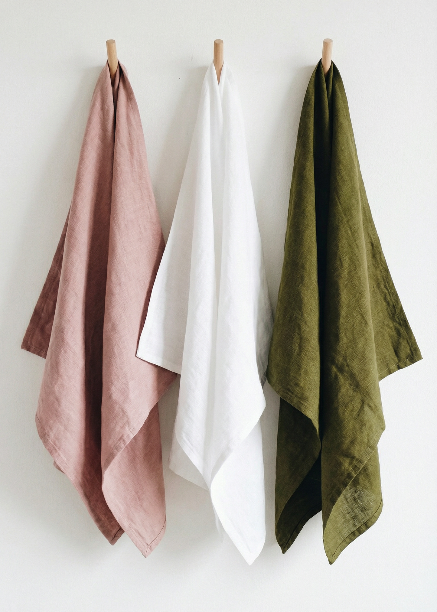 Three towels in pink, white, and green hanging on a white wall.