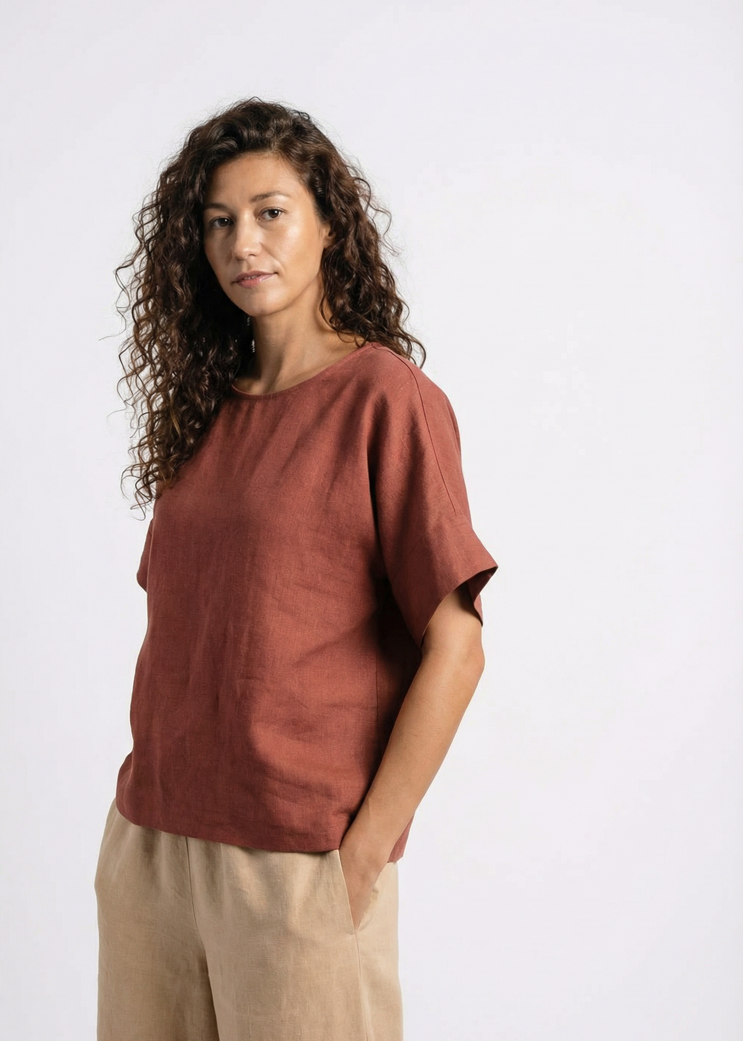 Woman wearing a rust-colored top and beige pants on a white background