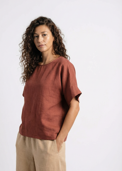 Woman wearing a rust-colored top and beige pants on a white background