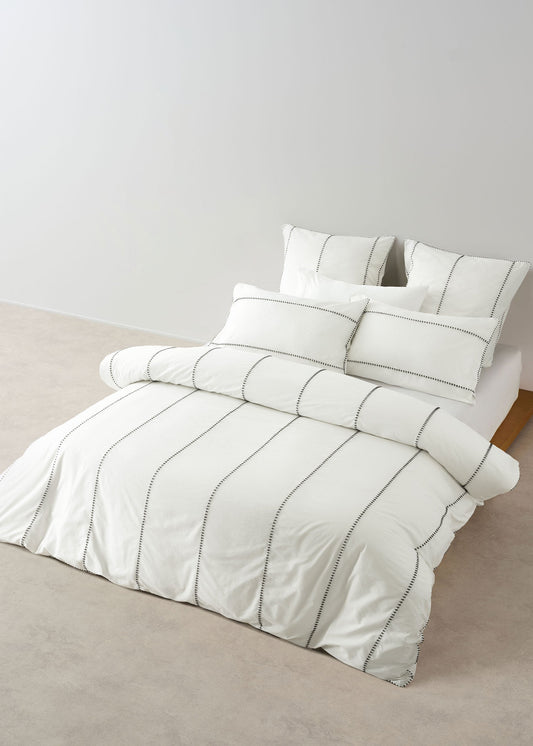 White bedding set with gray stripes on a bed against a plain wall.