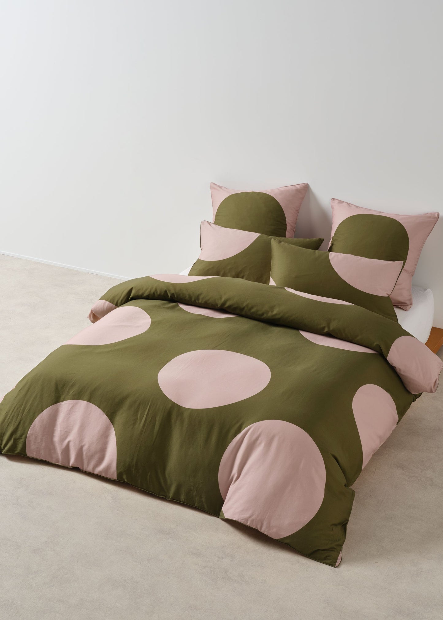 Green and pink polka dot bedding set on a bed with matching pillows.