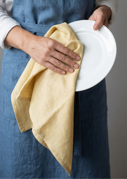 Person holding a white plate and beige cloth, wearing a blue apron.