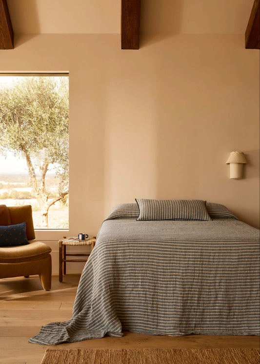 Bedroom with a bed covered in a striped duvet, a chair, and a window with a view of trees.
