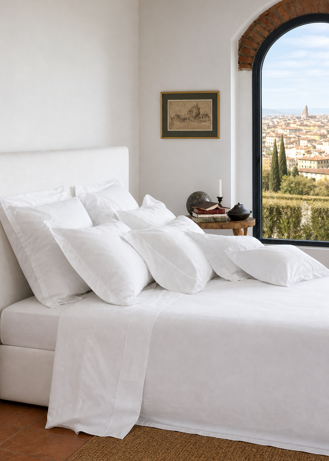 A neatly made bed with white bedding and multiple white pillows in a bright bedroom, with an arched window showing a scenic view and a small side table beside it.