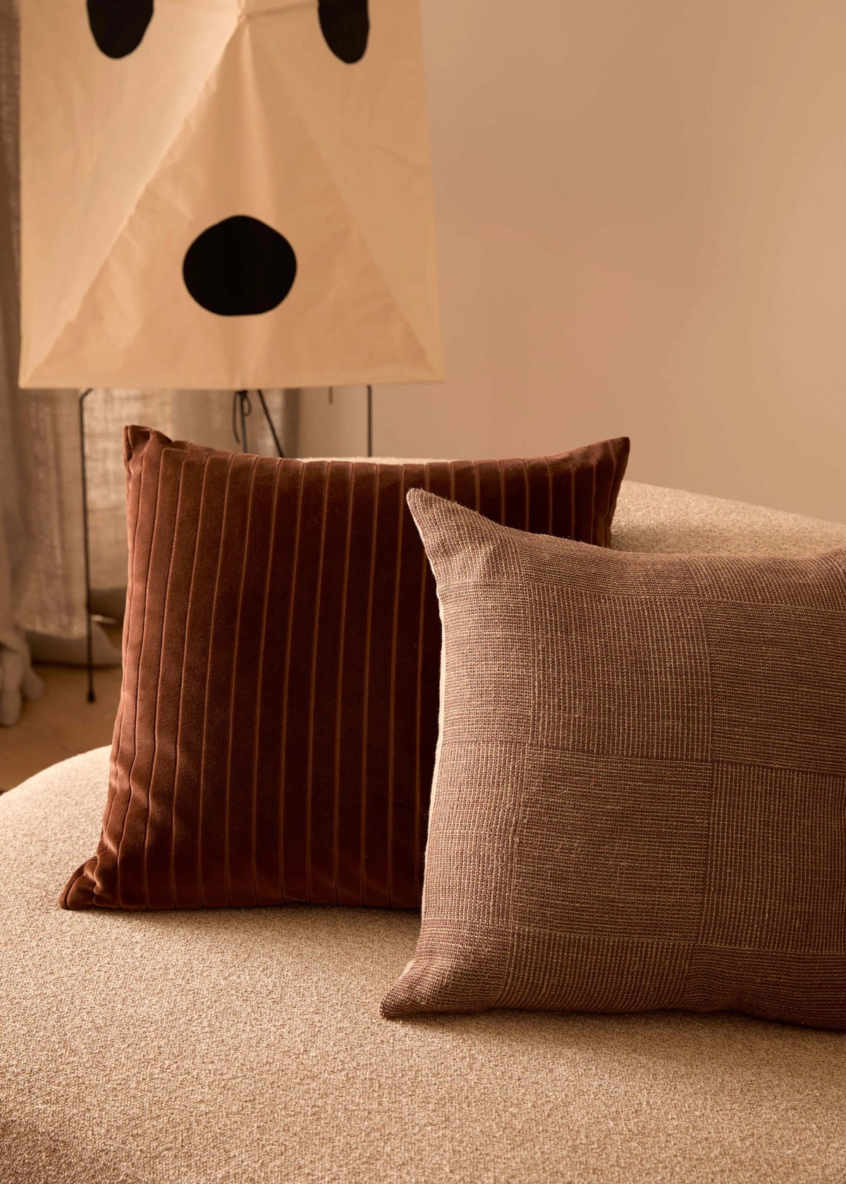 Two brown pillows on a beige sofa with a lamp in the background
