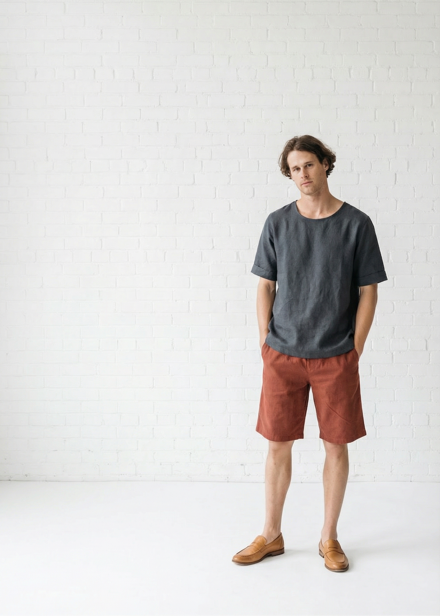 Man wearing a dark gray t-shirt and rust-colored shorts standing against a white background