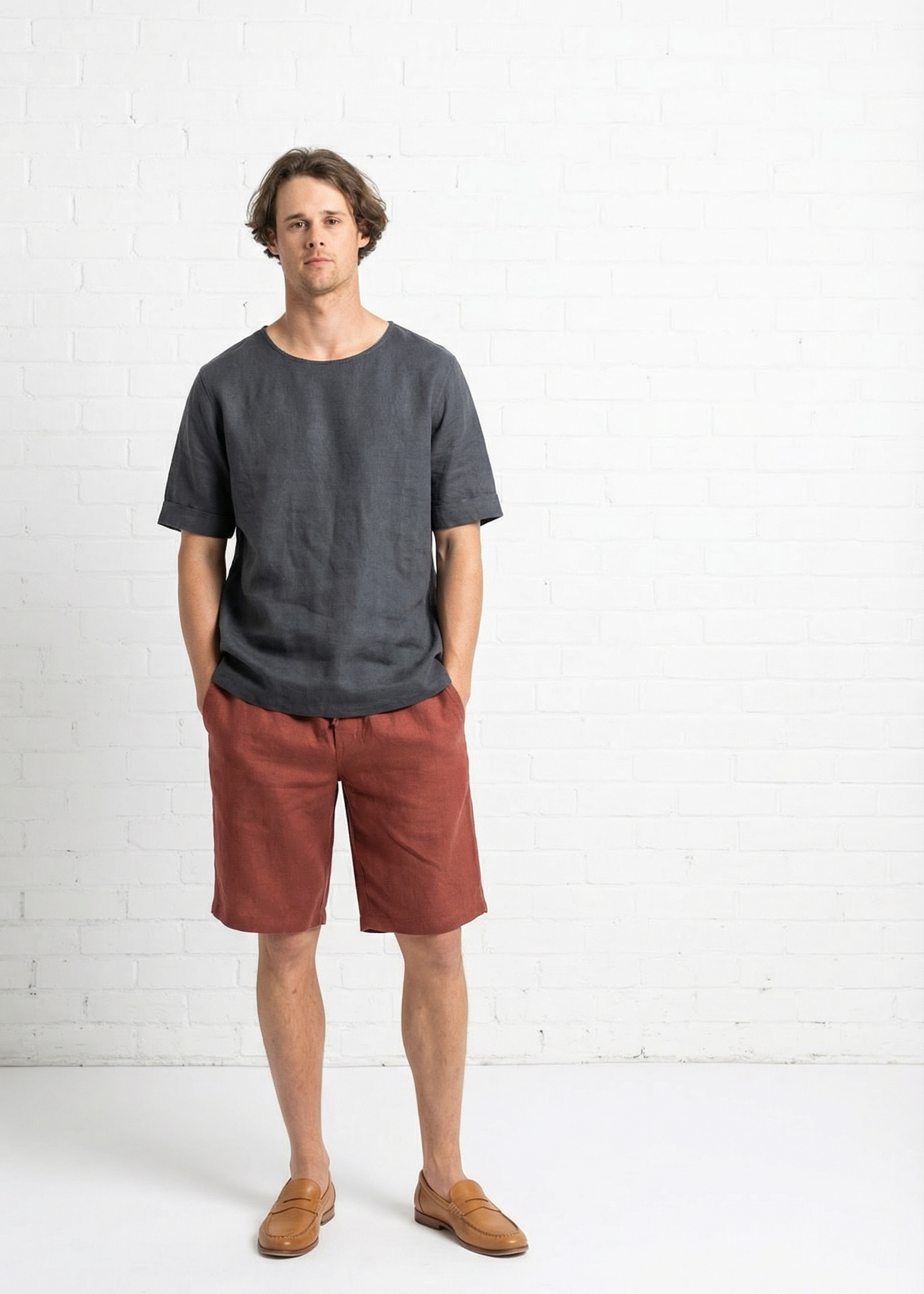 Man wearing a dark gray t-shirt and red shorts standing against a white background