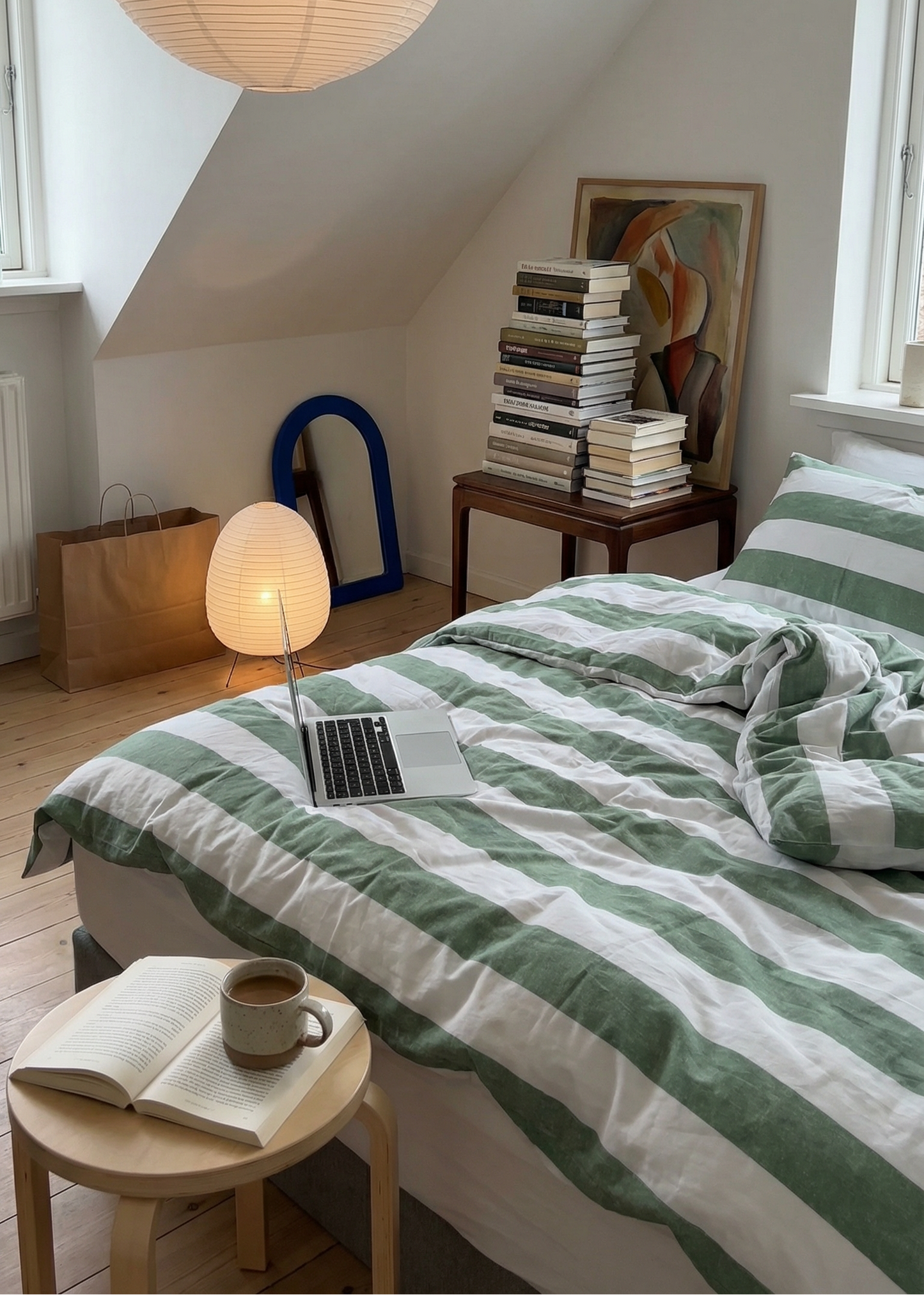 Cozy bedroom with green and white striped bedding, books, and a lamp.