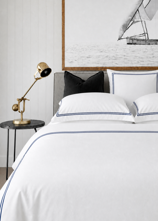 White bedding with blue piping on a bed in a bedroom setting.
