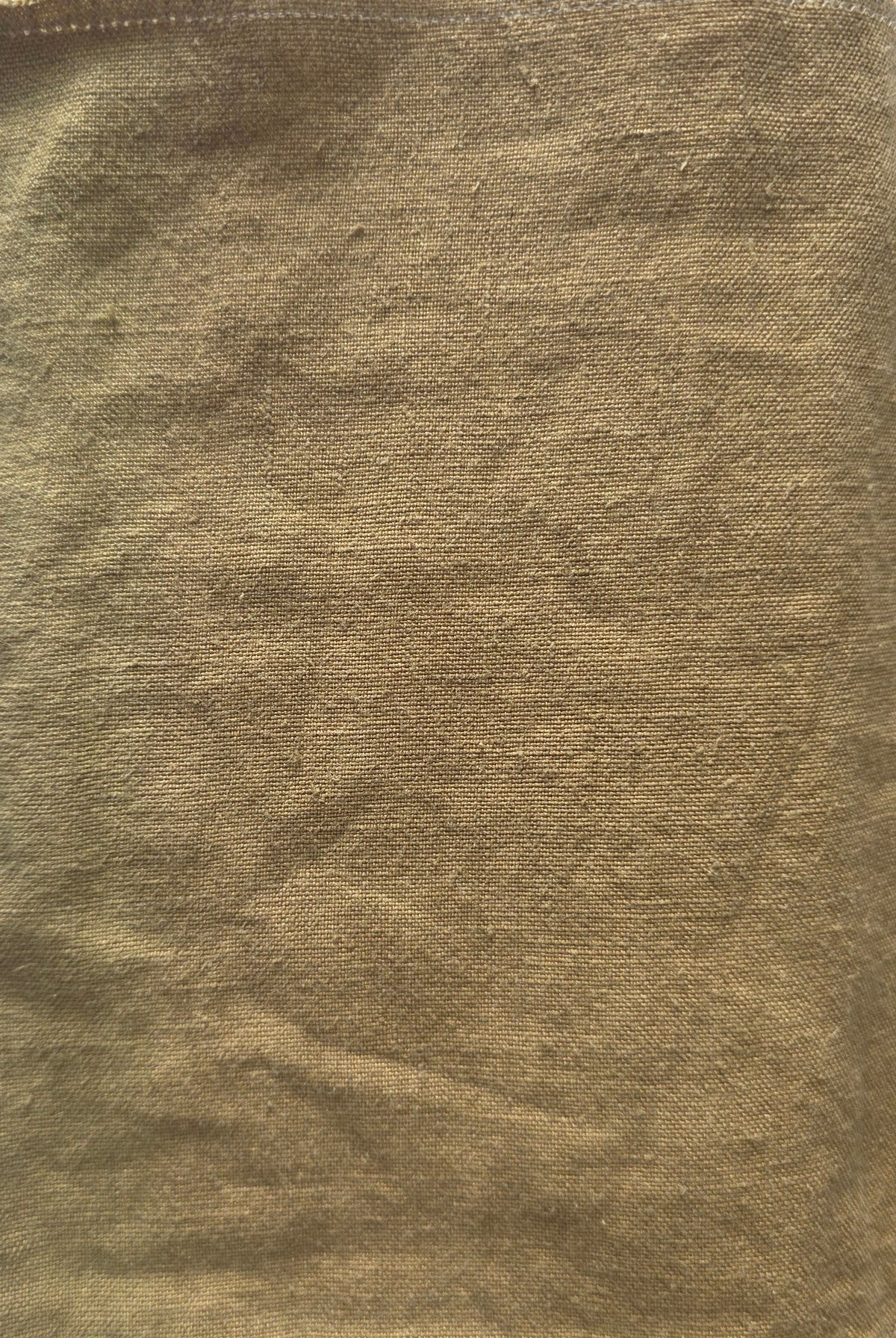 A square piece of textured tan or ochre-colored fabric laid flat on a white lined notebook page.