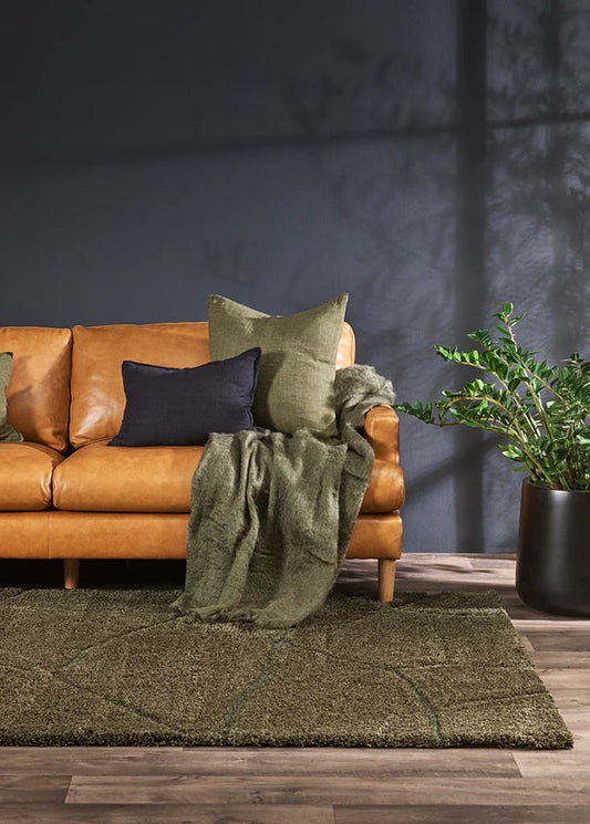 Brown leather sofa with green cushions and a blanket on a dark gray wall background