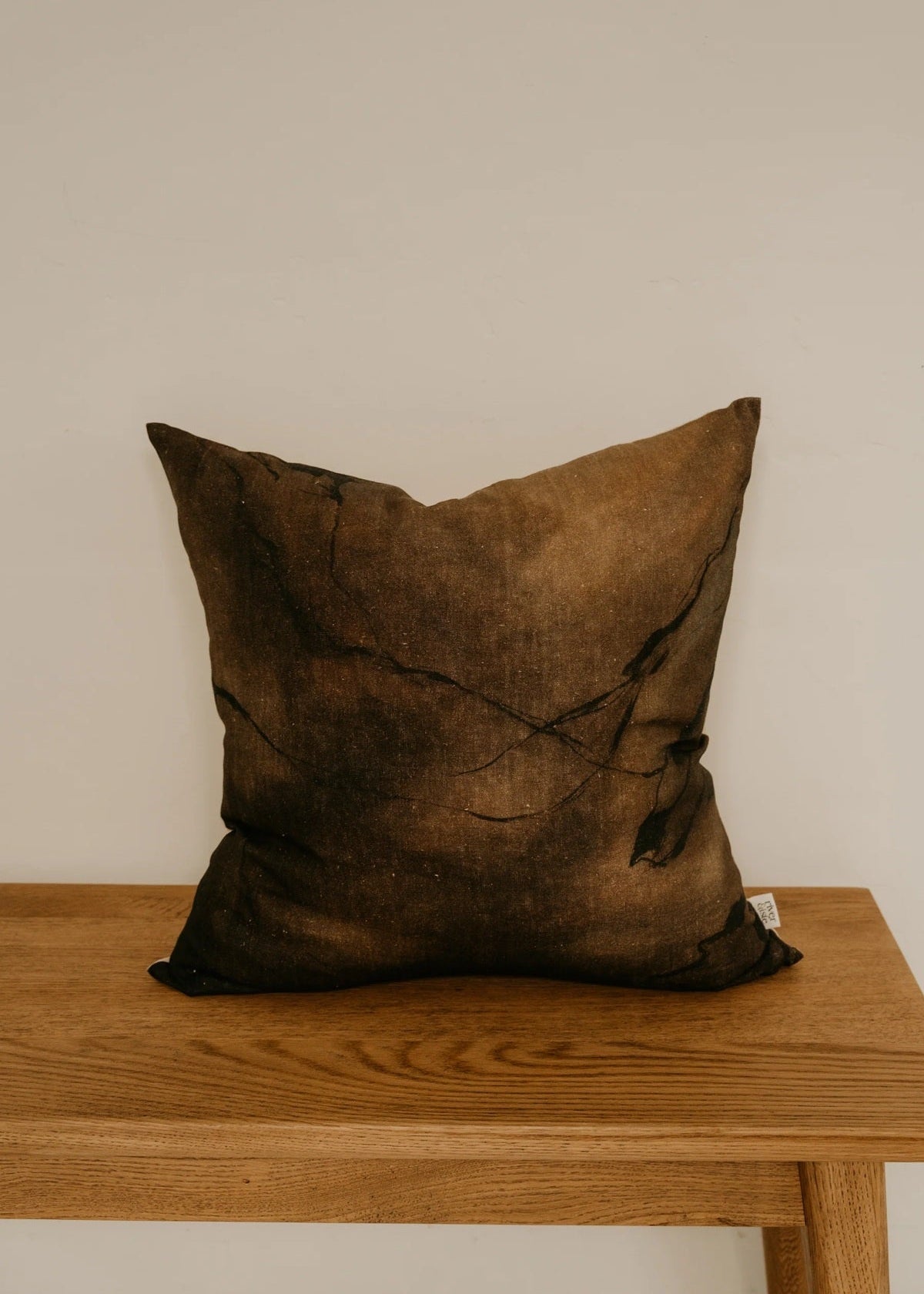 Brown textured pillow on a wooden table against a plain wall