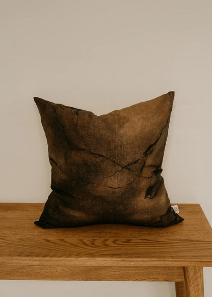 Brown textured pillow on a wooden table against a plain wall