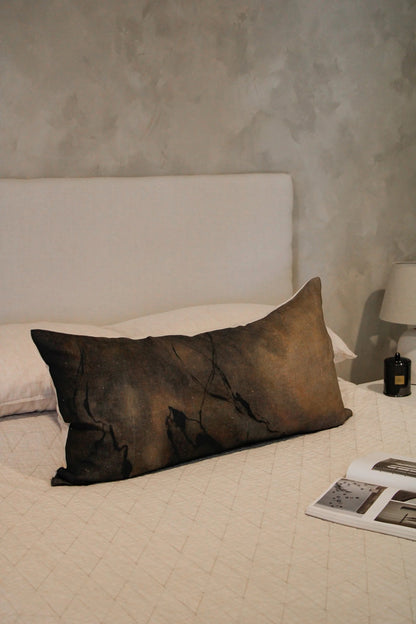 Brown pillow on a bed with a textured wall in the background