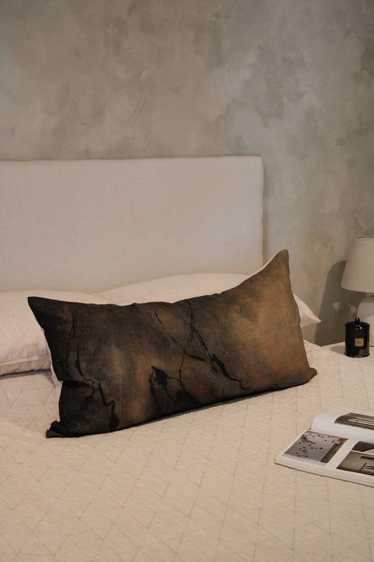 Brown pillow on a bed with a textured wall in the background