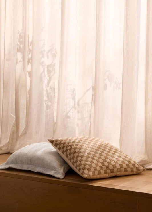 Two pillows on a wooden surface with sheer curtains in the background