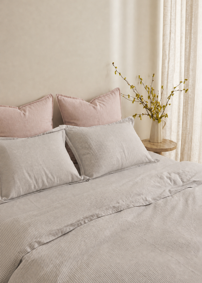 Neatly made bed with light gray bedding and pink pillows in a softly lit room.
