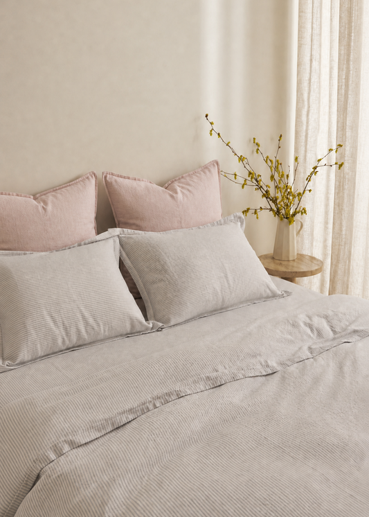 Neatly made bed with light gray bedding and pink pillows in a softly lit room.
