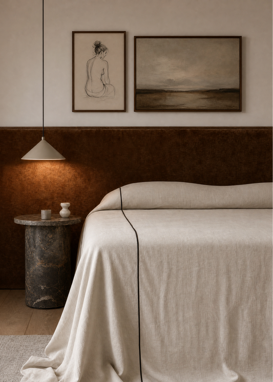 Neatly made bed with beige bedding in a bedroom setting, featuring wall art and a side table.