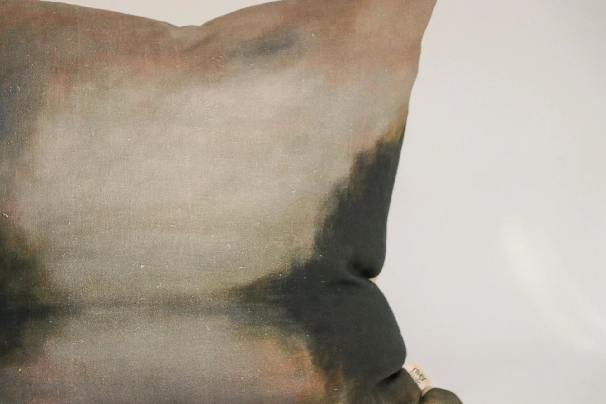 A close-up of a square throw pillow featuring a painterly, textured print with blended shades of gray, brown, beige, and dark charcoal.