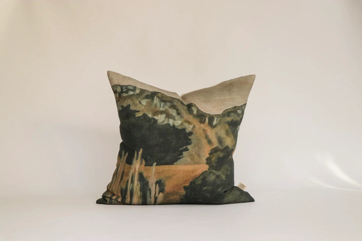 A square decorative throw pillow featuring a scenic landscape print with dark green trees, a winding beige path, and a light beige top border, set against a plain off-white background.