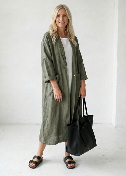 Woman wearing a long green coat holding a black bag on a white background