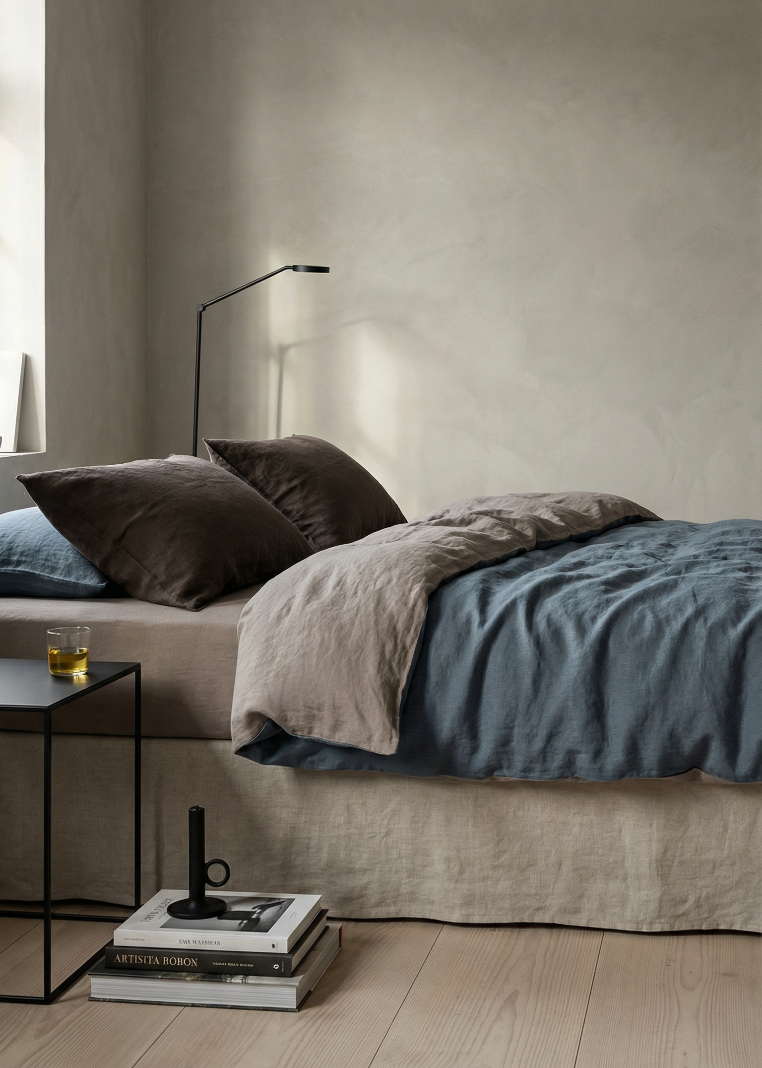 Modern bedroom with a bed, side table, and lamp against a neutral wall.