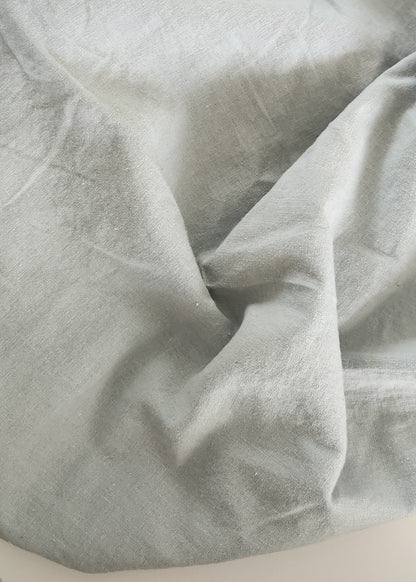 A light gray fabric bag or pouch made of a soft, slightly wrinkled material, draped over a white rectangular surface on a dark gray carpeted floor.