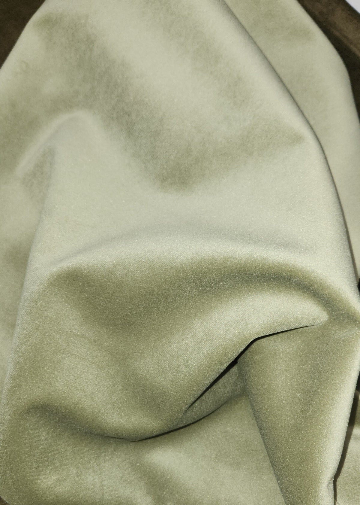 A close-up of draped fabric in a muted sage green color, showing its soft texture and folds.