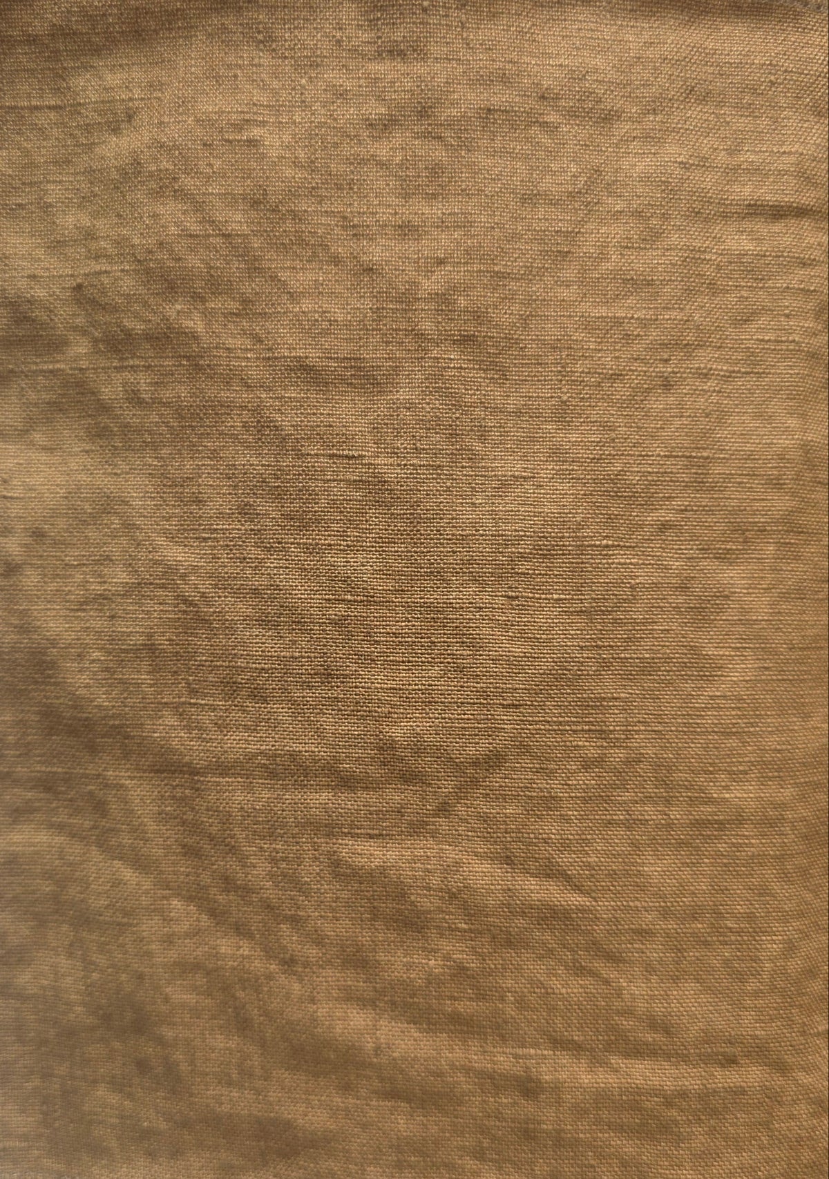 A square piece of textured tan fabric with frayed edges, laid flat on a white surface.