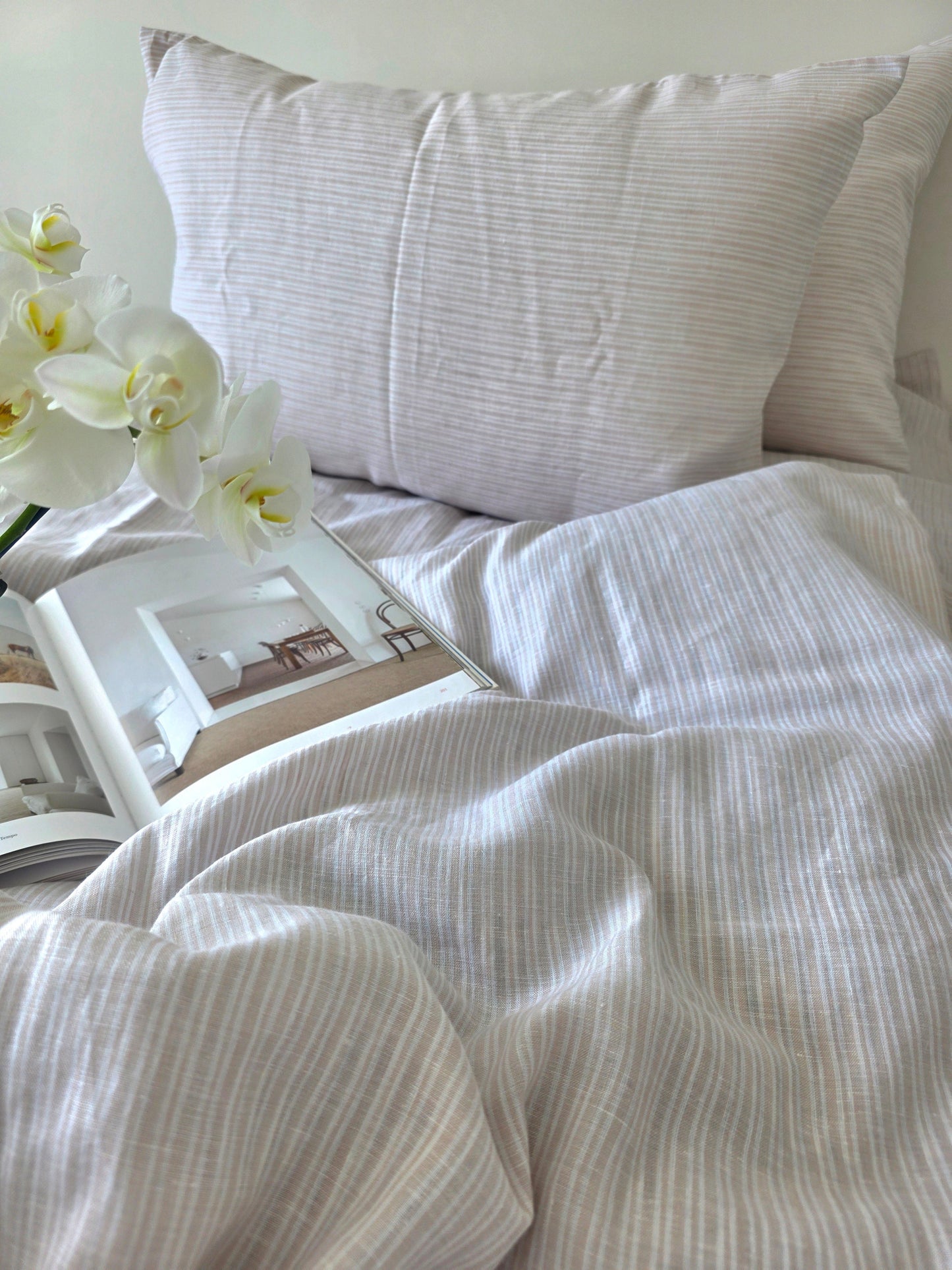 Neatly made bed with white bedding and a pillow, featuring a framed picture and white orchids.