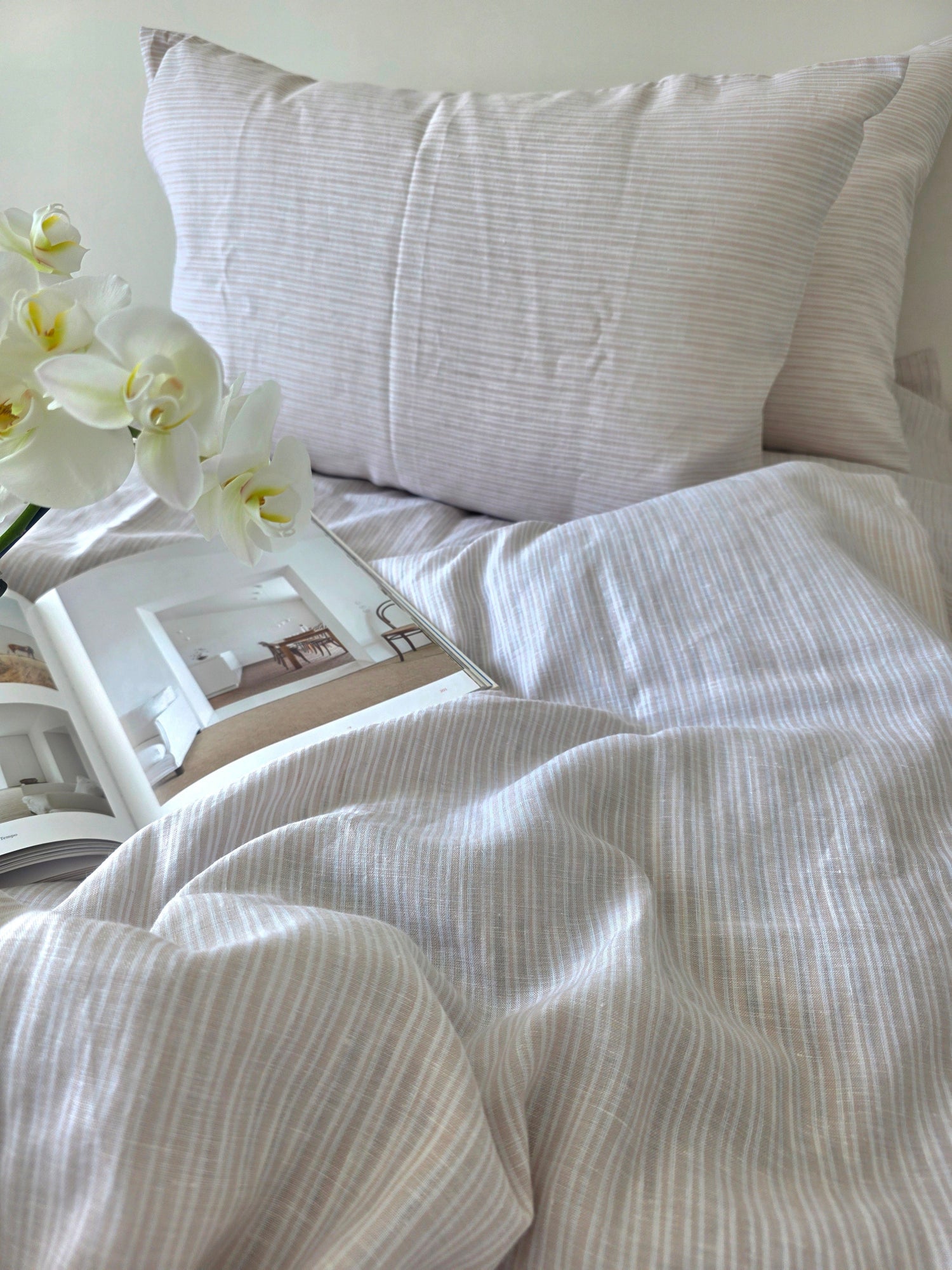Neatly made bed with white bedding and a pillow, featuring a framed picture and white orchids.