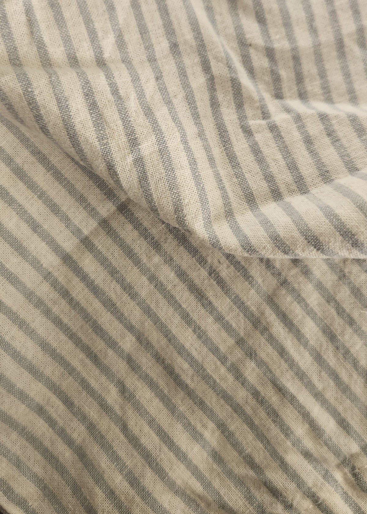 Close-up of a striped fabric with vertical beige and gray stripes, showing a soft woven texture and gentle folds.