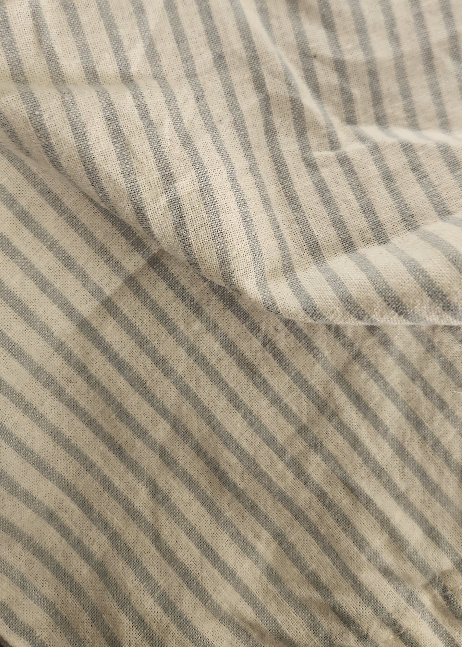 Close-up of a striped fabric with vertical beige and gray stripes, showing a soft woven texture and gentle folds.