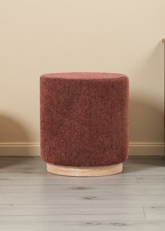 Round brown ottoman on a wooden floor next to a cabinet.
