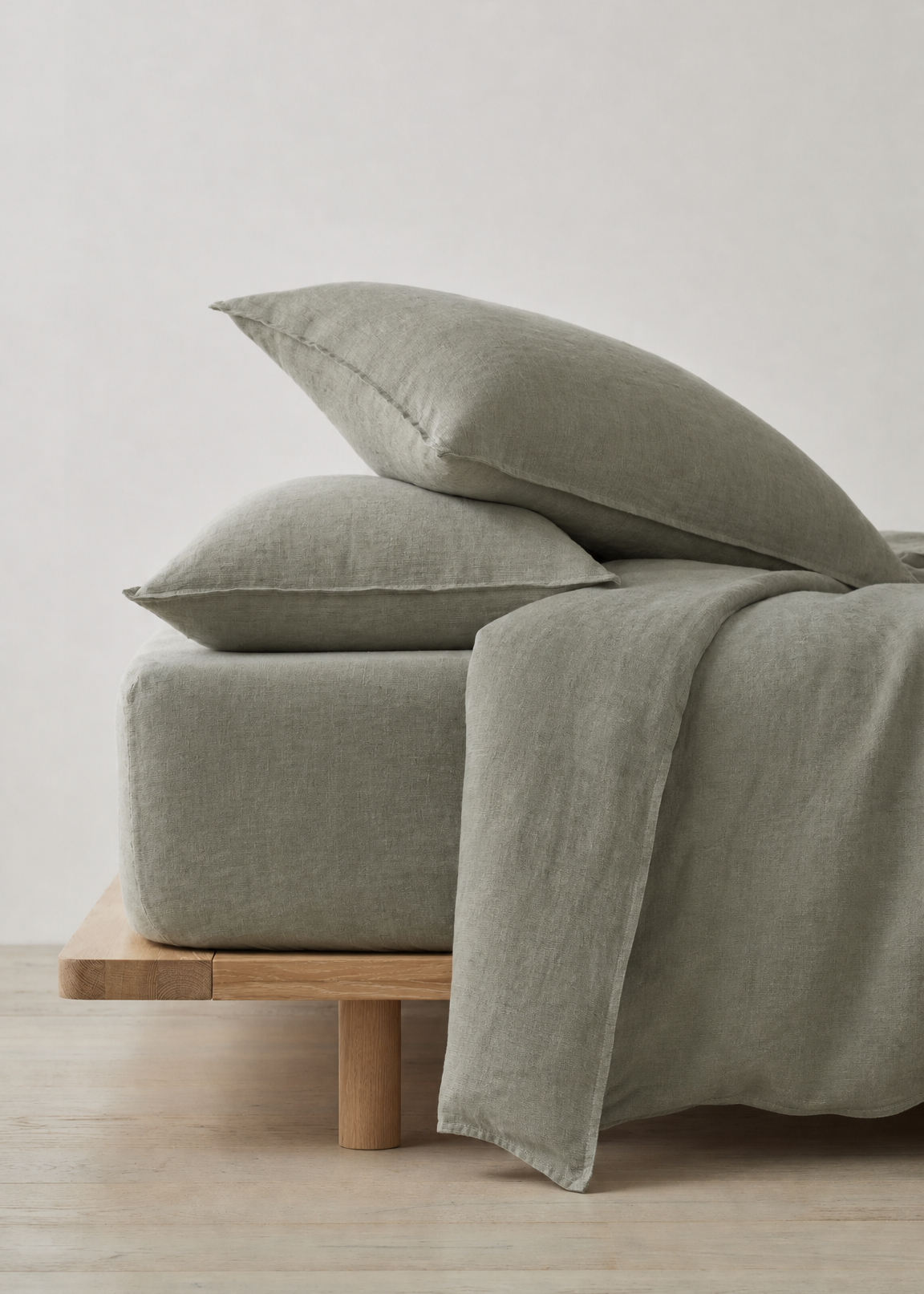 Green bedding set on a wooden bed frame against a light gray wall.
