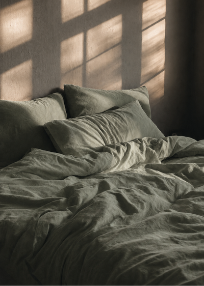 Bed with green bedding and pillows in a dimly lit room with sunlight filtering through.