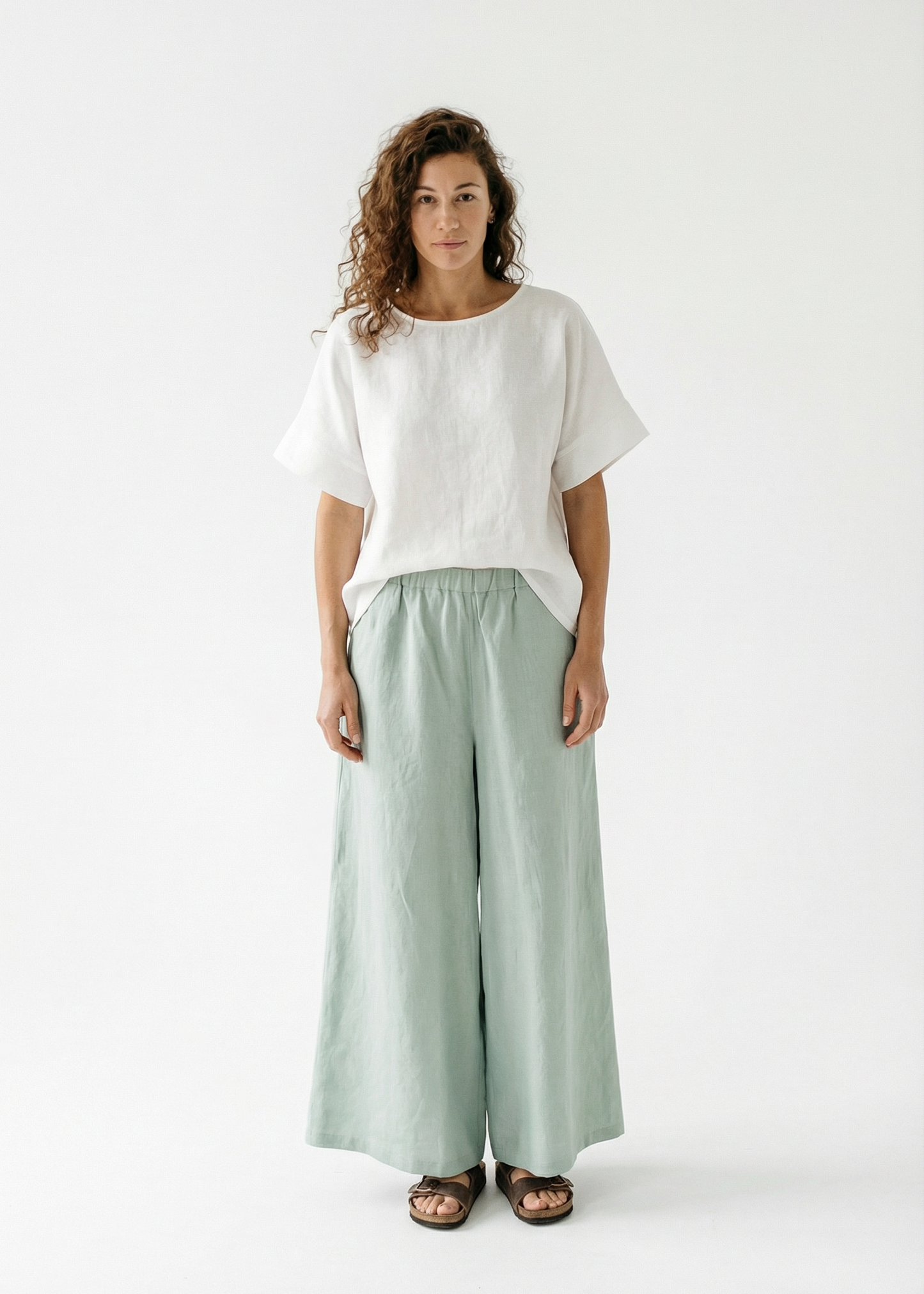 Woman wearing a white top and light green pants on a white background