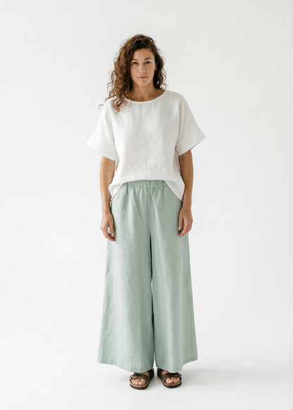 Woman wearing a white top and light green pants on a white background