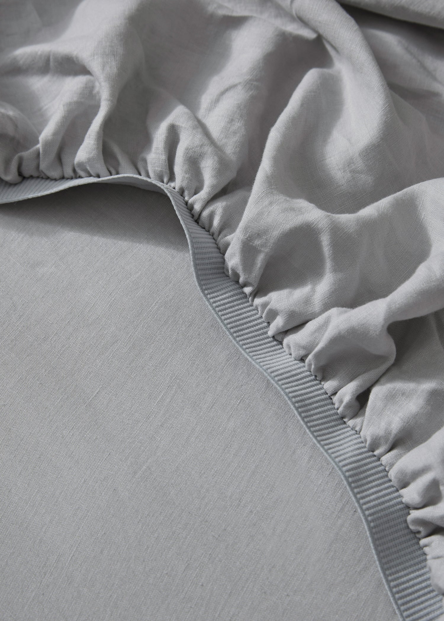 Close-up of a silver French flax linen fitted sheet on a mattress, showing the woven texture and elastic band.