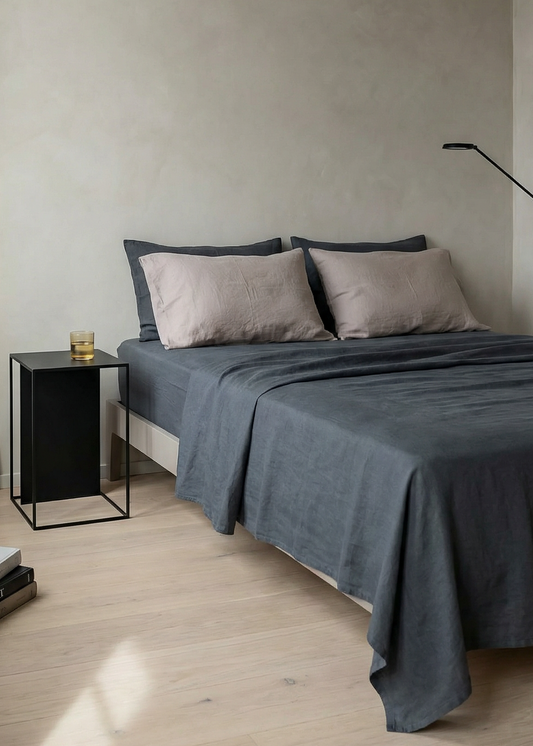 Minimalist bedroom with a bed, side table, and lamp against a plain wall.