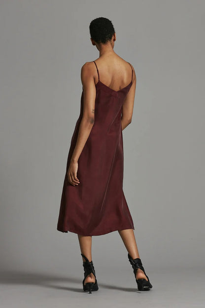 Woman wearing a burgundy slip dress against a gray background