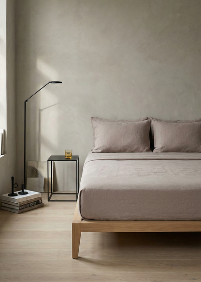 Modern bedroom with a bed, side table, and lamp against a plain wall.