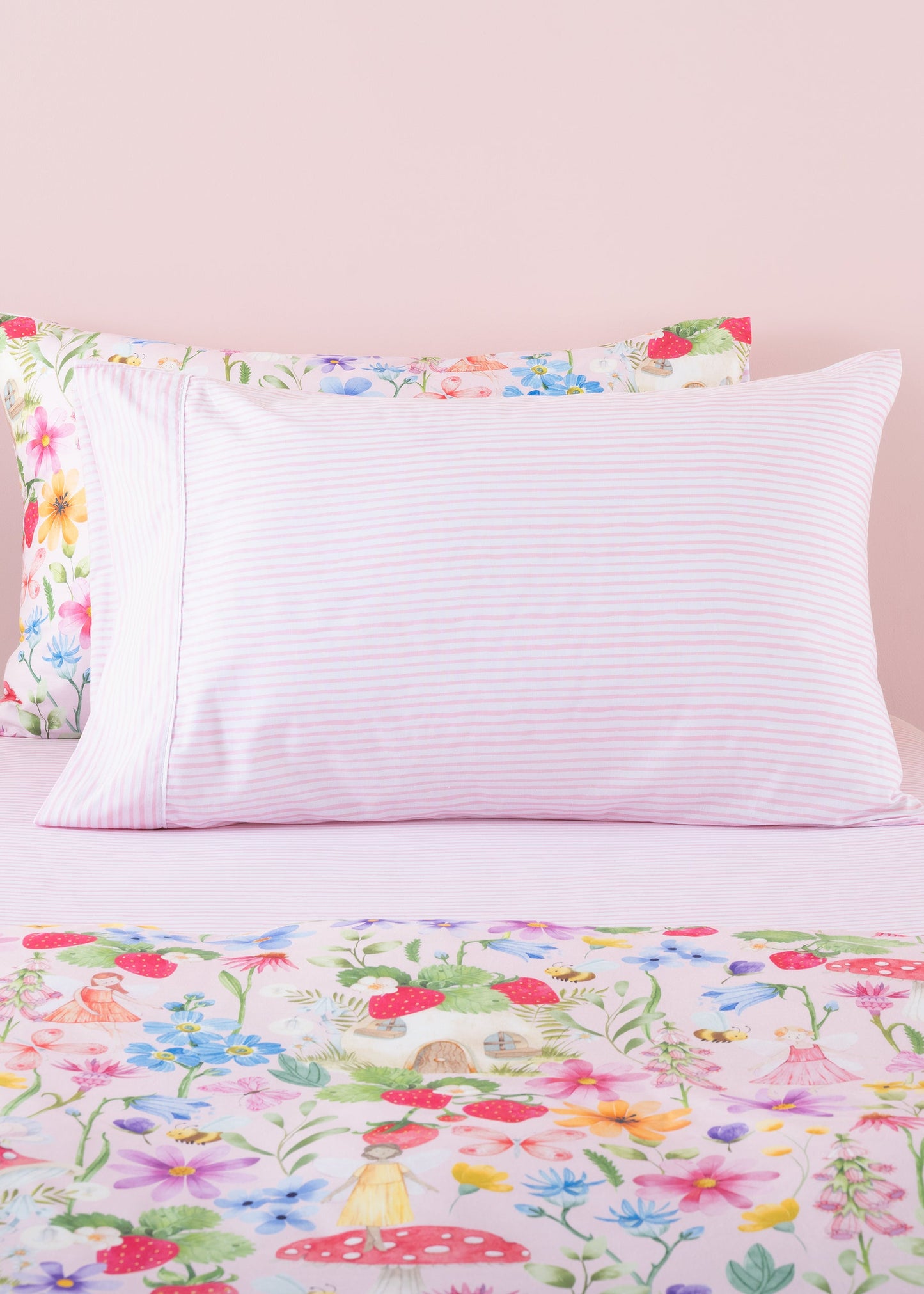 Floral bedspread and striped pillow on a bed with a light pink background