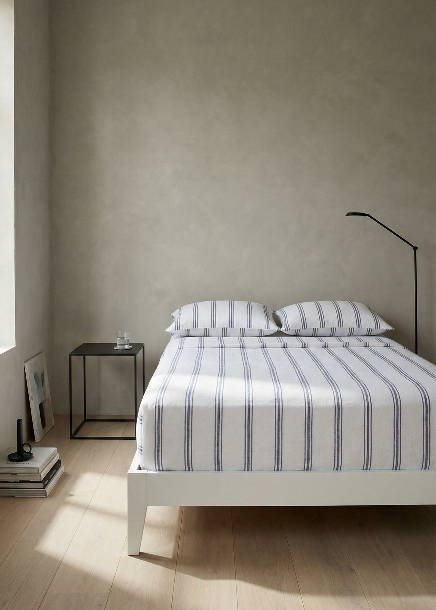 Minimalist bedroom with a bed, nightstand, and lamp against a plain wall.