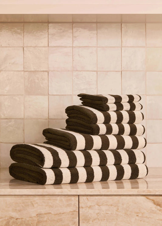 Stack of brown and white striped towels on a tiled bathroom shelf.