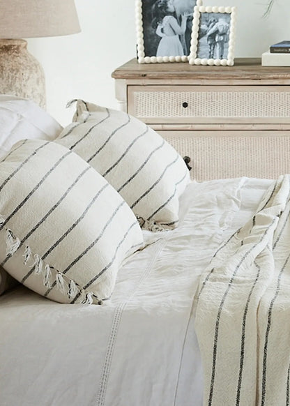 Neatly made bed with striped bedding and pillows, dresser in the background.